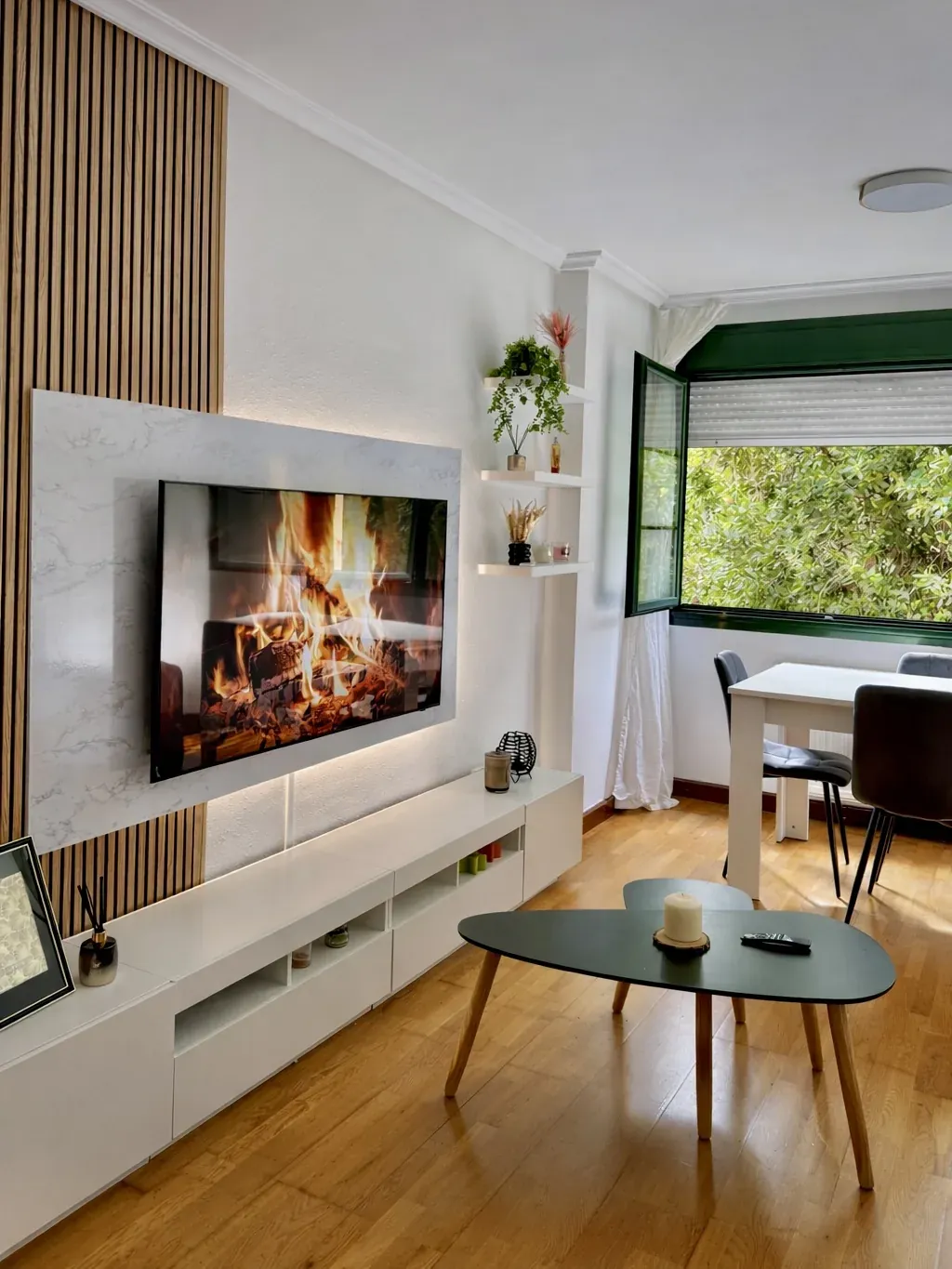 Salón principal con TV, chimenea decorativa y ventana al fondo